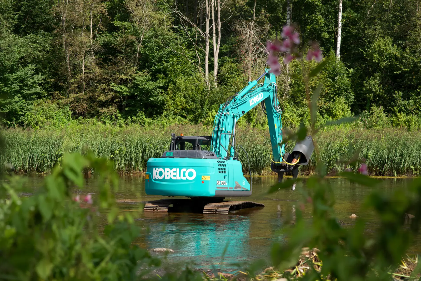 Kobelco Kettenbagger der SK130-Baureihe arbeitet in einem Gewässer am Waldrand