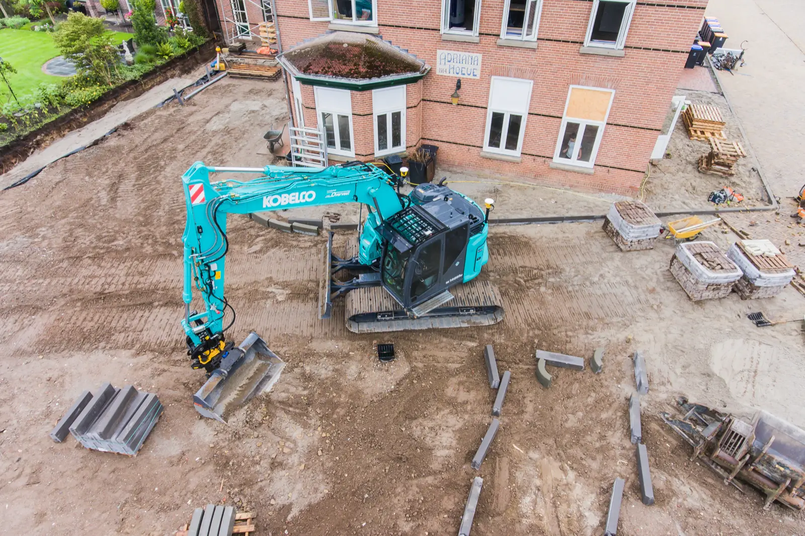 Kobelco SK140SRLC auf einer Baustelle vor einem Backsteingebäude, von oben