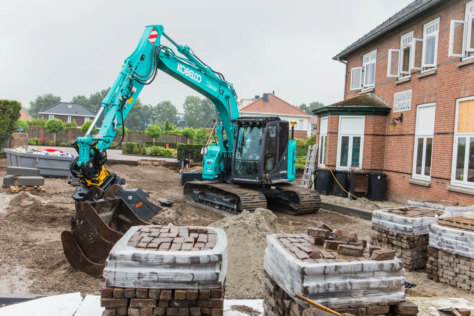 Kobelco SK140SRLC neben Paletten mit Pflastersteinen