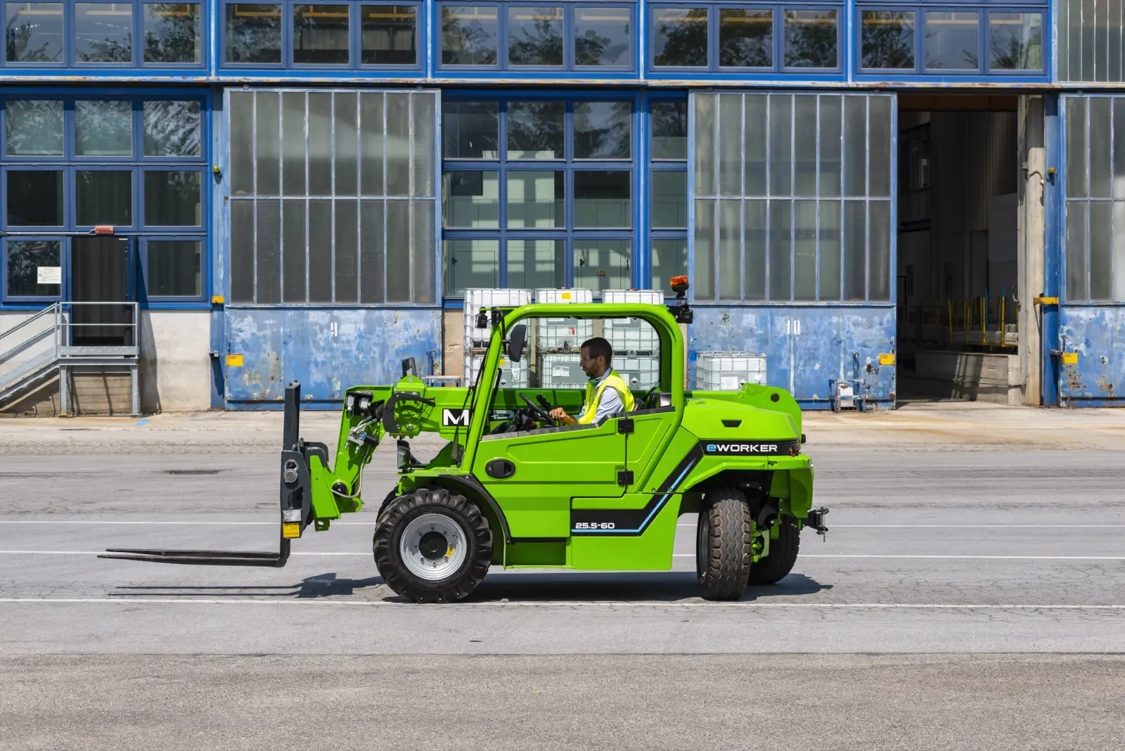 Merlo eWorker EW 25.5-60 mit Lastgabeln fährt vor einer Werkshalle
