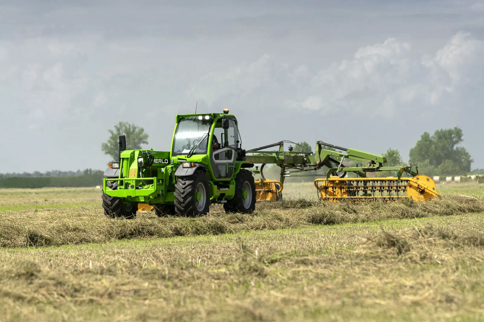 Baureihenbild zu Merlo MF 34.7 CS-140-CVTRONIC: Merlo Multifarmer MF 34 mit angebautem Heuwender auf einer Wiese