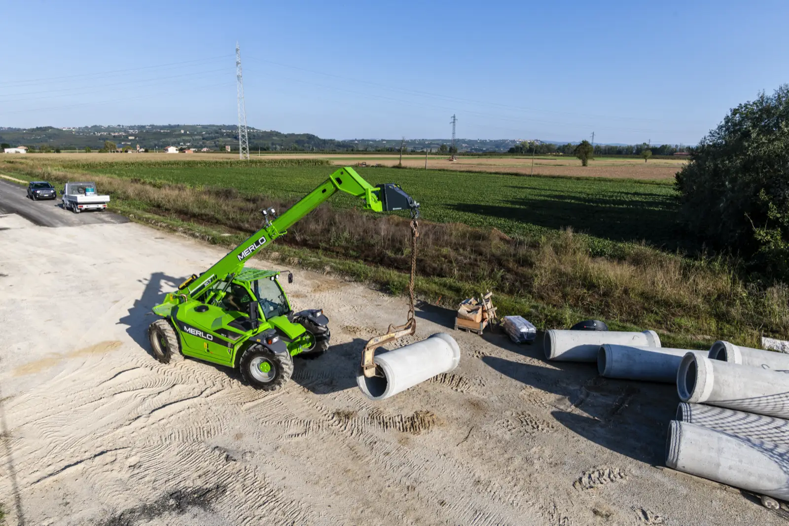 Merlo P30.7 hebt ein Betonrohr am Lasthaken auf einer Kiesfläche
