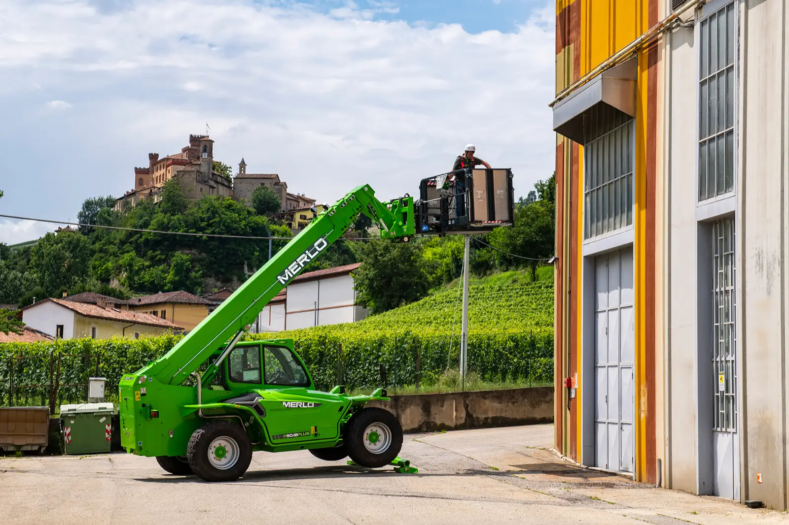 Merlo Panoramic 50.18 mit Gitterbox am Arm vor einem gelben Gebäude