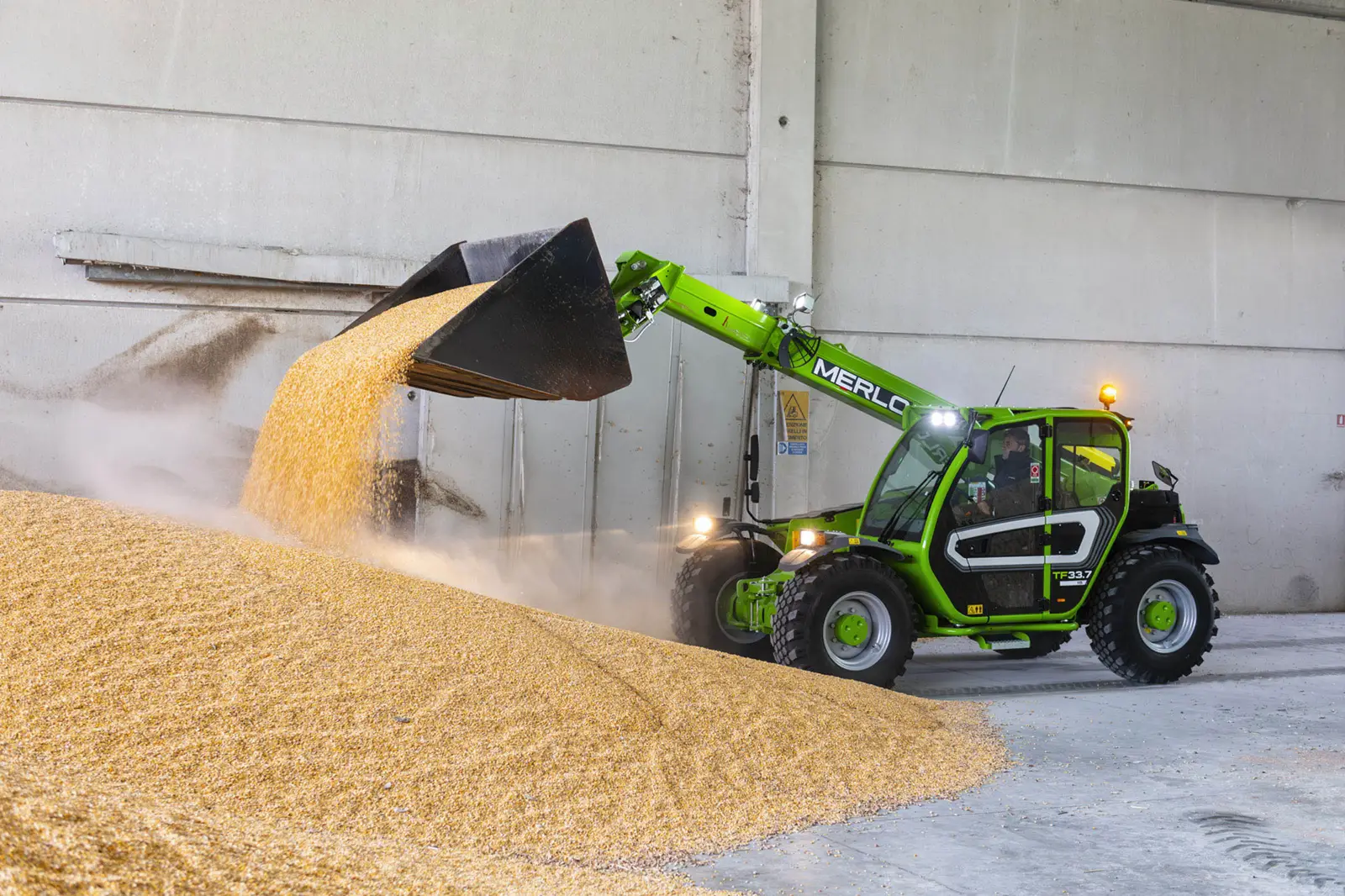 Baureihenbild zu Merlo TF 33.7 G: Merlo TF33.7 schüttet mit der Schaufel Getreide in einer Halle auf