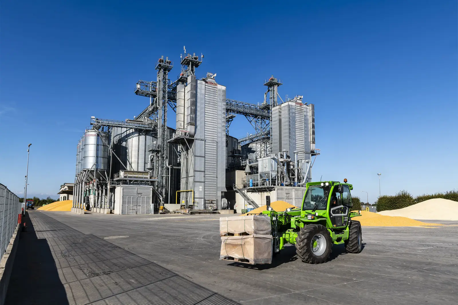Baureihenbild zu Merlo TF 42.7 CS-136-CVTRONIC: Merlo TF42.7 fährt eine Palette über einen Platz vor Getreidesilos