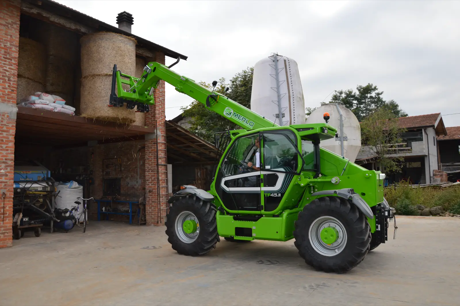 Baureihenbild zu Merlo TF 45.11 T-170-HF: Merlo TF45.11 mit Palettengabel auf einer Hofstelle vor alten Silos
