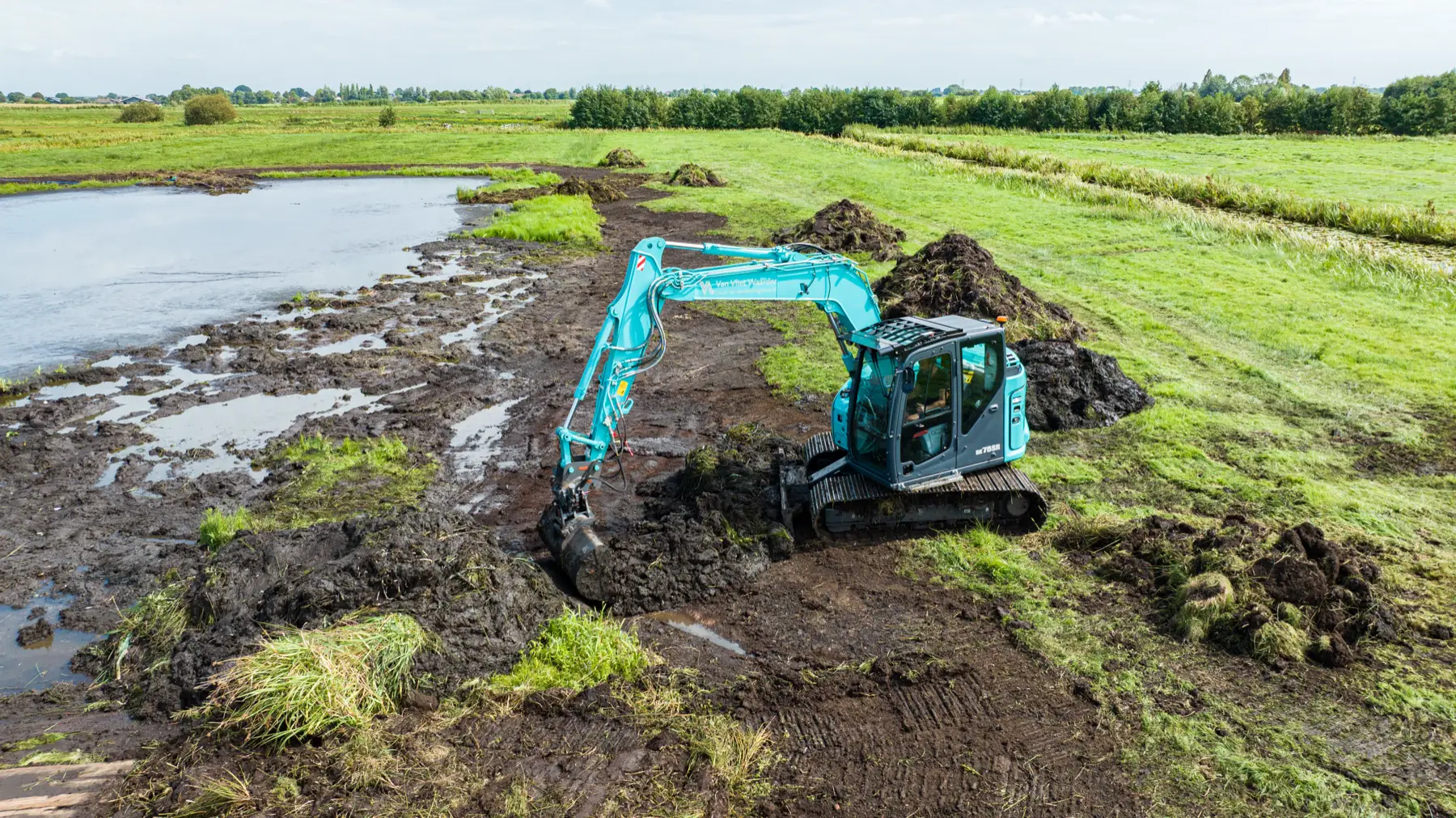 Kobelco SK75SR bei Erdarbeiten auf einer nassen Wiese, von oben