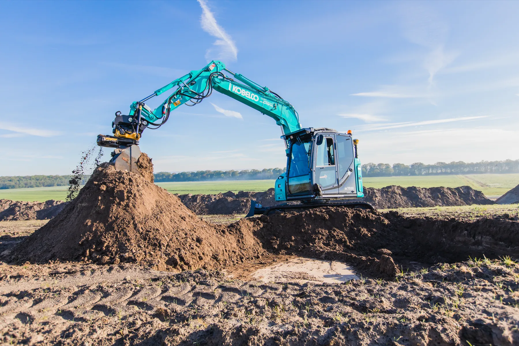 Kobelco SK75SR mit Tiltrotator an einem Erdhaufen auf einer Baustelle