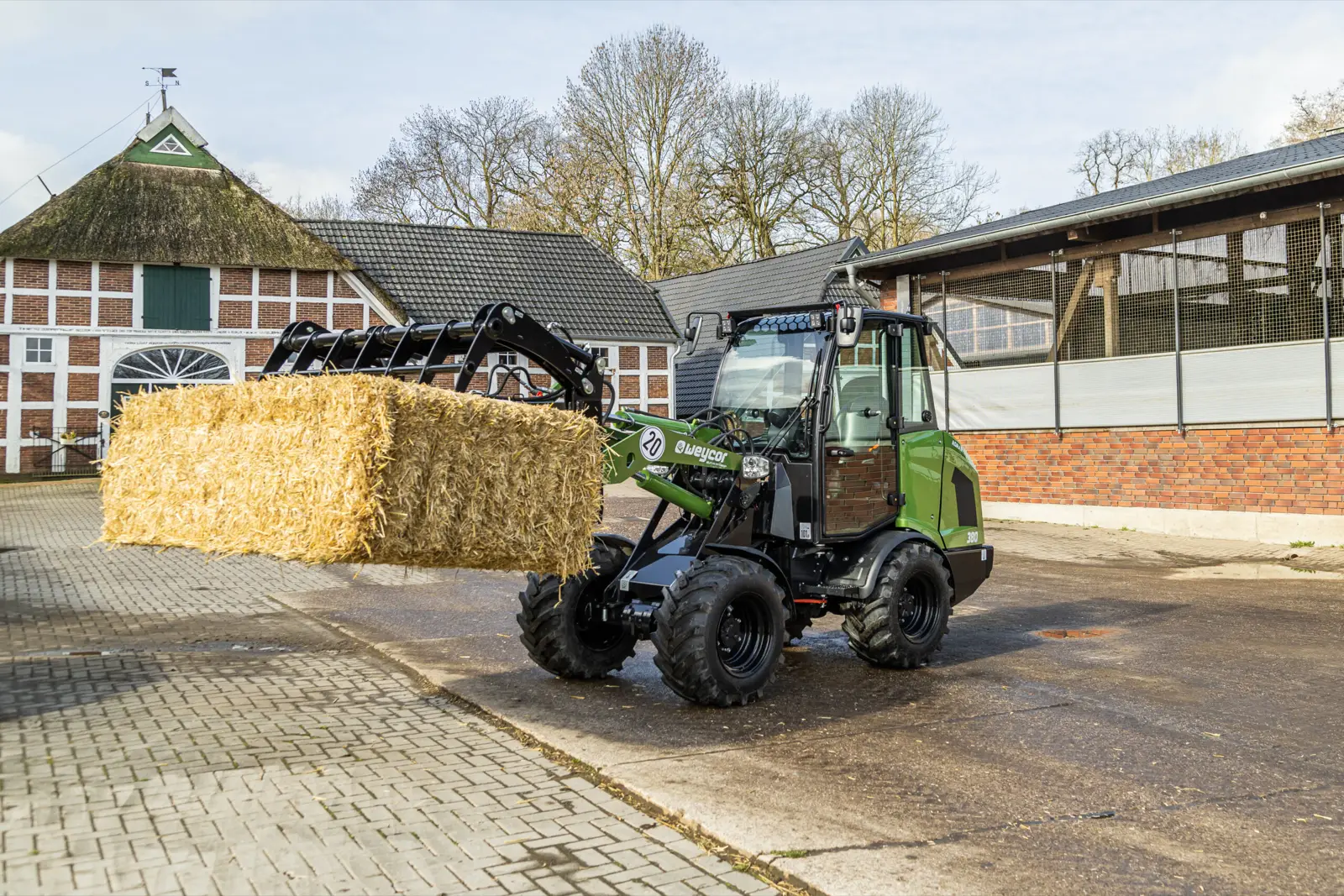 Baureihenbild zu Weycor Agrarline 360: Weycor Agrarline Radlader der 3er-Serie transportiert einen Strohballen vor einem Bauernhaus