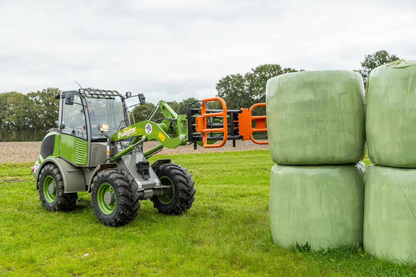 Weycor AR400 Agrarline mit Ballenzange neben gewickelten Rundballen