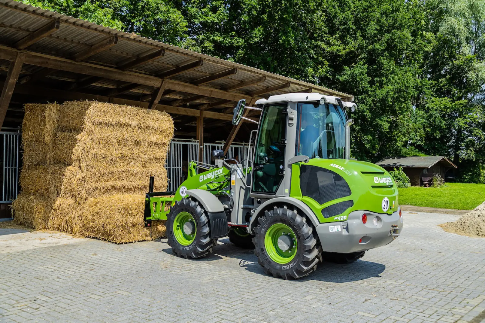 Weycor AR420 Agrarline mit Strohballen vor einem Backsteinstall