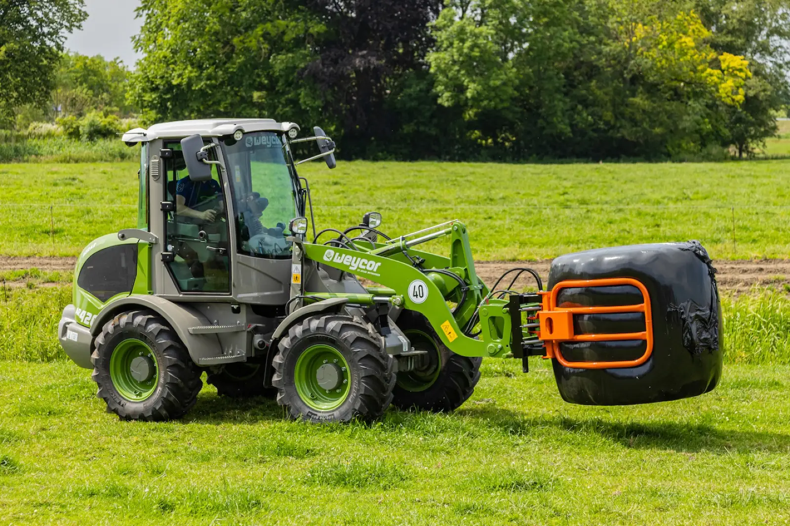 Weycor AR420 Agrarline trägt einen Rundballen mit der Ballenzange
