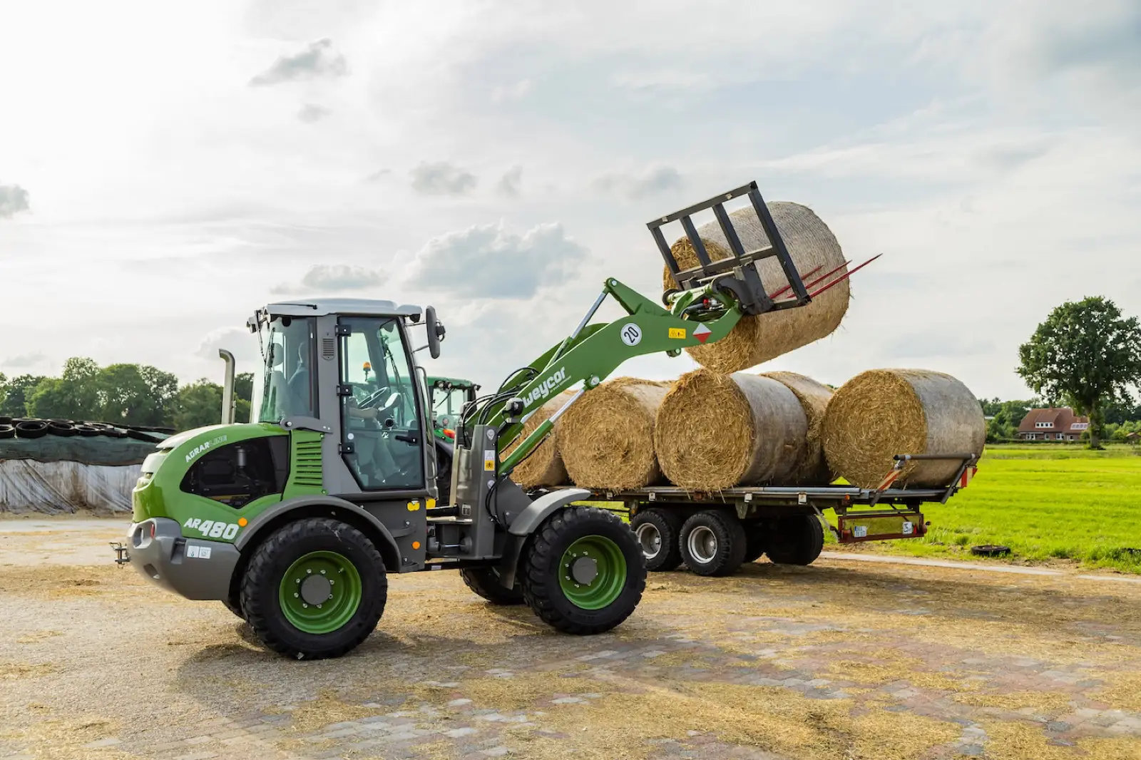 Weycor AR480 Agrarline hebt einen Rundballen auf einen Ballenwagen