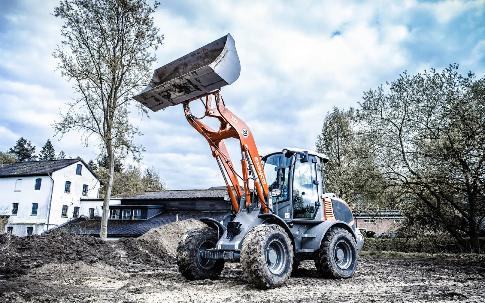 Weycor AR480 mit angehobener Schaufel neben einem Baum