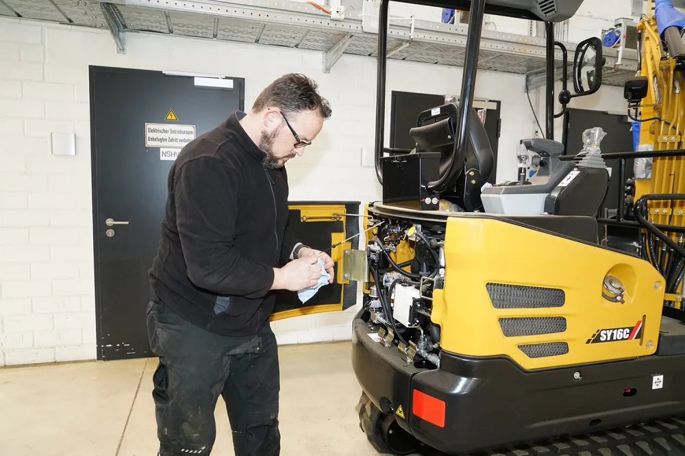 Monteur von Rossow Baumaschinen prüft den Ölstand an einem Minibagger in der Werkstatt