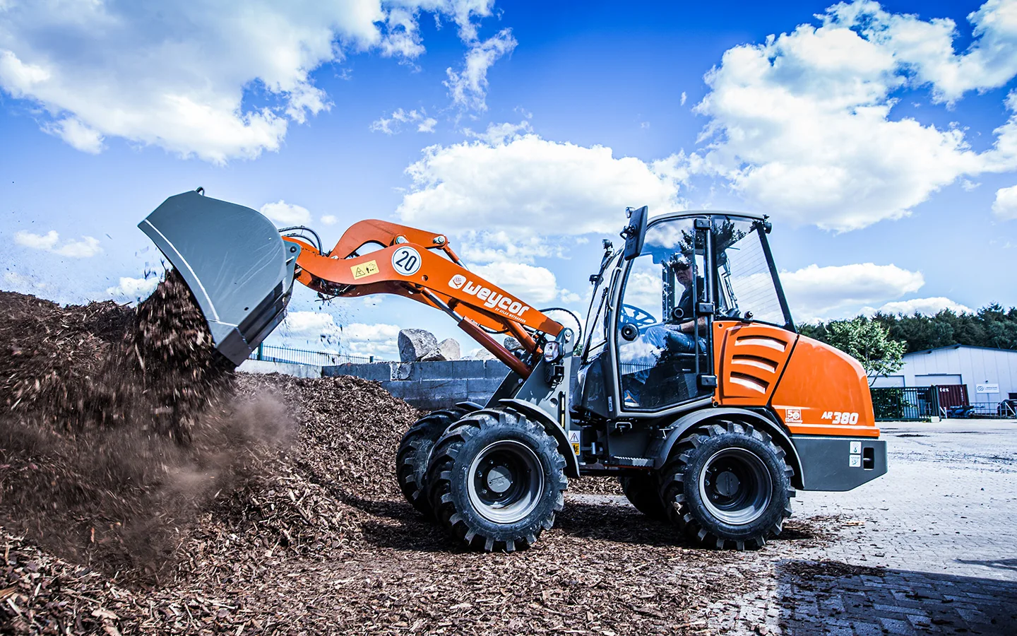 Orangefarbener Weycor-Radlader AR 380 schüttet mit der Schaufel Holzhackschnitzel auf eine Halde